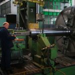 Adult male worker inspecting large machinery in an industrial factory setting.