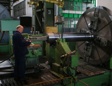 Adult male worker inspecting large machinery in an industrial factory setting.