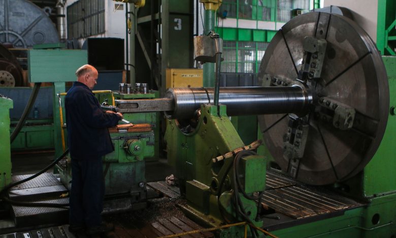 Adult male worker inspecting large machinery in an industrial factory setting.