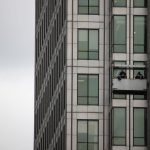 Two workers cleaning windows on a high-rise building facade in an urban environment.