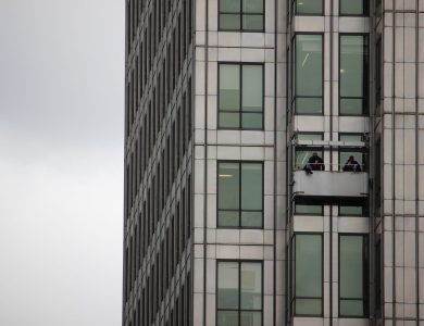 Two workers cleaning windows on a high-rise building facade in an urban environment.