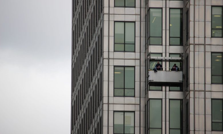 Two workers cleaning windows on a high-rise building facade in an urban environment.