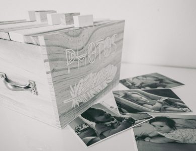Black and white photo of a wooden box labeled 'Photos' with scattered family prints.