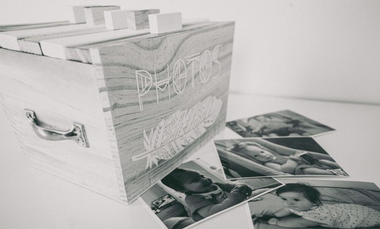 Black and white photo of a wooden box labeled 'Photos' with scattered family prints.