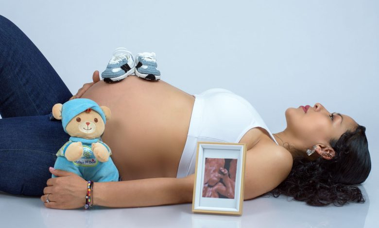 Pregnant woman lying with baby shoes, ultrasound photo, and teddy bear. Beautiful maternity imagery.