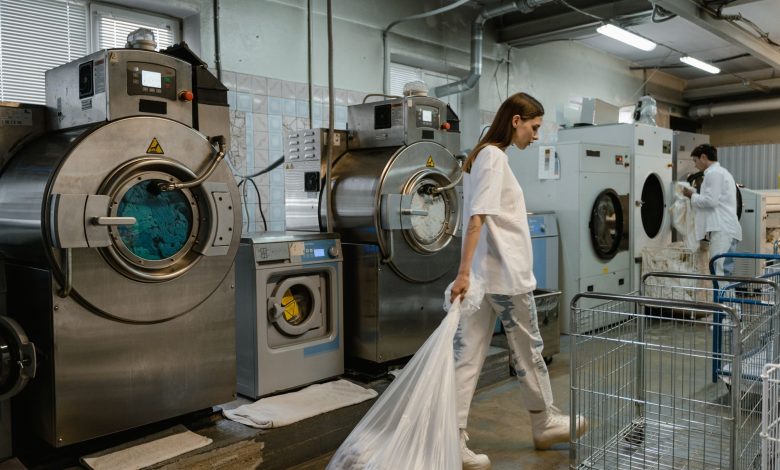 Busy industrial laundry with workers handling large washing machines.