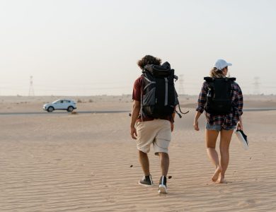A couple walking in a vast desert with backpacks, heading towards the horizon.
