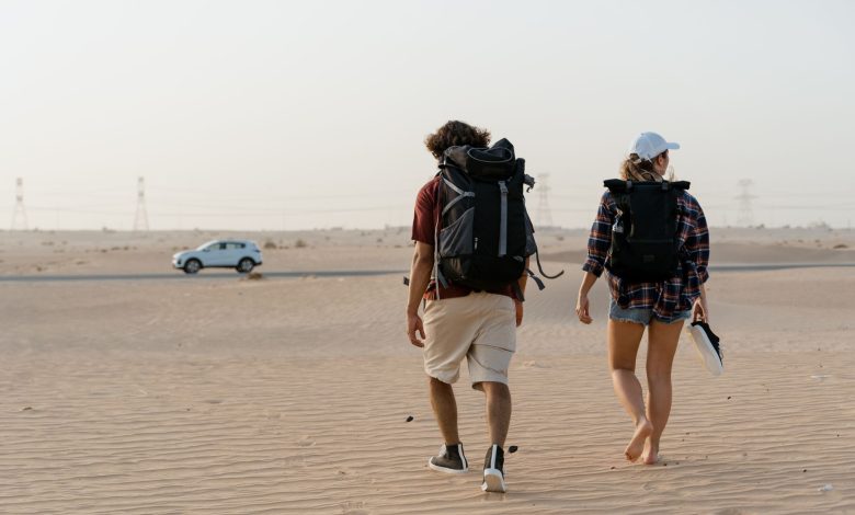 A couple walking in a vast desert with backpacks, heading towards the horizon.