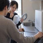 Over the shoulder of one of two renters in a compact apartment kitchenette, the foreground renter