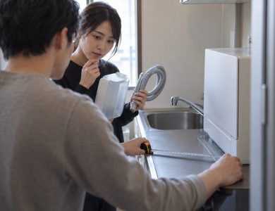 Over the shoulder of one of two renters in a compact apartment kitchenette, the foreground renter