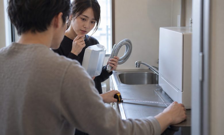 Over the shoulder of one of two renters in a compact apartment kitchenette, the foreground renter