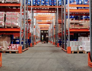 A spacious industrial warehouse with stocked shelves and a worker in protective gear.
