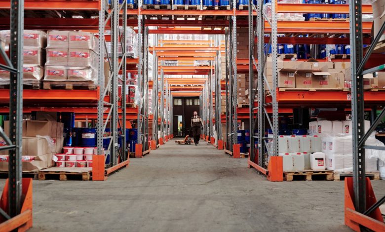 A spacious industrial warehouse with stocked shelves and a worker in protective gear.