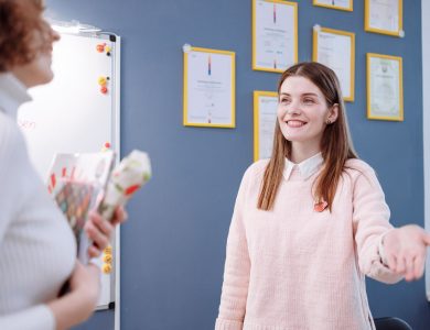 Smiling woman in a pink sweater engaging in conversation in an office environment.