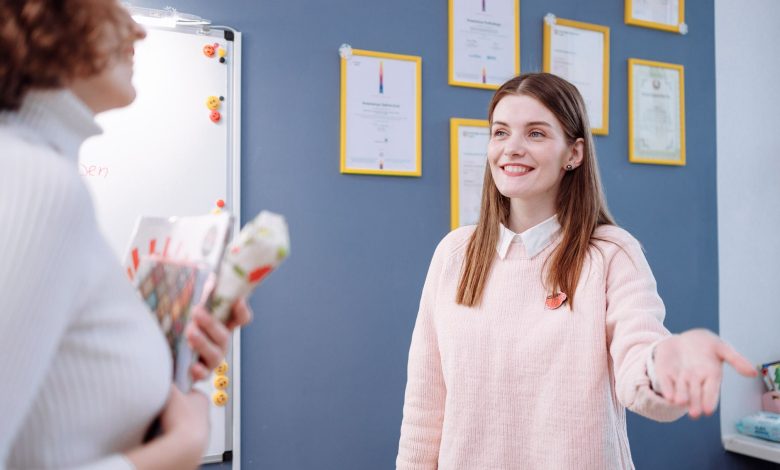 Smiling woman in a pink sweater engaging in conversation in an office environment.