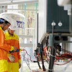 Two technicians with helmets working on electrical equipment outdoors, ensuring safety.
