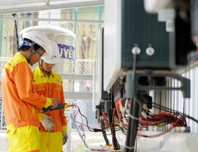 Two technicians with helmets working on electrical equipment outdoors, ensuring safety.