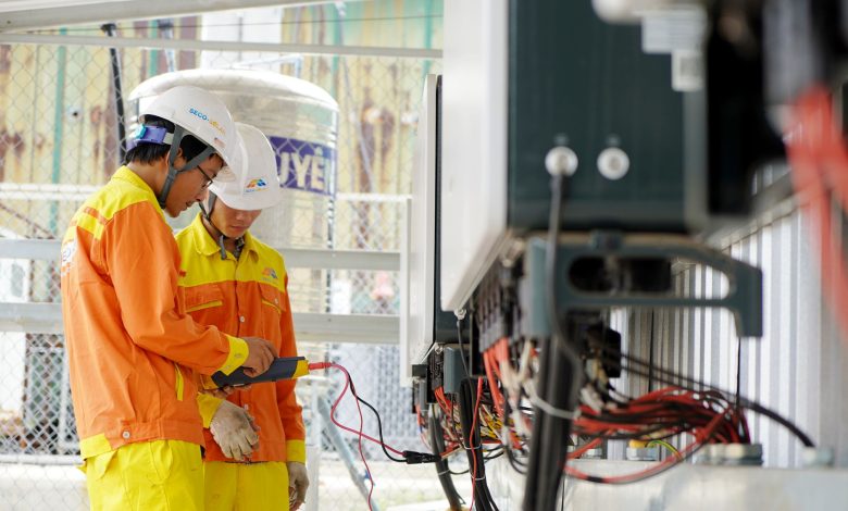 Two technicians with helmets working on electrical equipment outdoors, ensuring safety.
