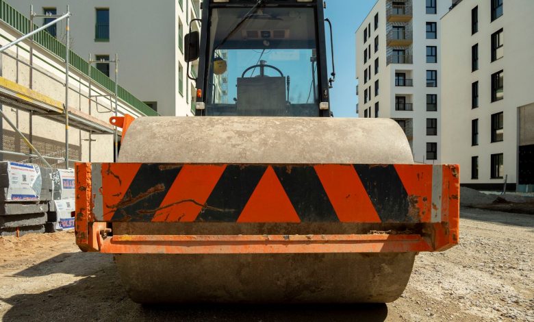 Close-up of a steamroller on a construction site in Wrocław, Poland with modern buildings in the background.