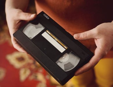 A person holds a vintage VHS tape against a warm, patterned background, evoking nostalgia.