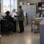 Two people are in a compact accounts-payable room at a Canadian building-supply wholesaler: an AP clerk