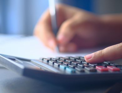 A close-up image of hands working on a calculator and writing, representing budgeting and financial planning.