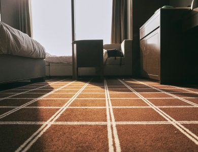 Low-angle view of a sunlit bedroom with patterned carpet and modern furniture, creating a warm atmosphere.