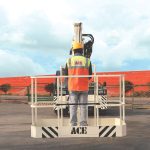 A worker in safety gear operates an ACE man lift crane, showcasing industrial safety in an outdoor setting.