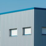 A sleek industrial building with a corrugated metal facade featuring roller blinds and sandwich panels.