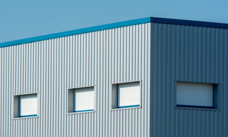 A sleek industrial building with a corrugated metal facade featuring roller blinds and sandwich panels.