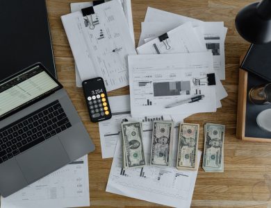 Overhead view of financial documents, cash, and technology on a wooden desk.