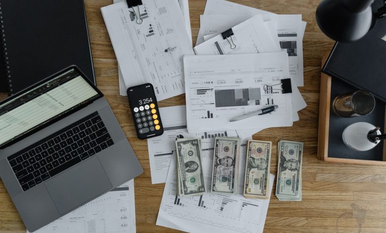Overhead view of financial documents, cash, and technology on a wooden desk.