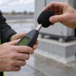 On an unfinished commercial roof beside the plinth for a new air-handling unit, a facilities project