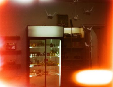 Dimly lit shop interior featuring a refrigerated display and hanging paper cranes.