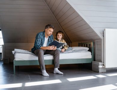 A father and son sharing a bonding moment while reading a book in an attic bedroom.