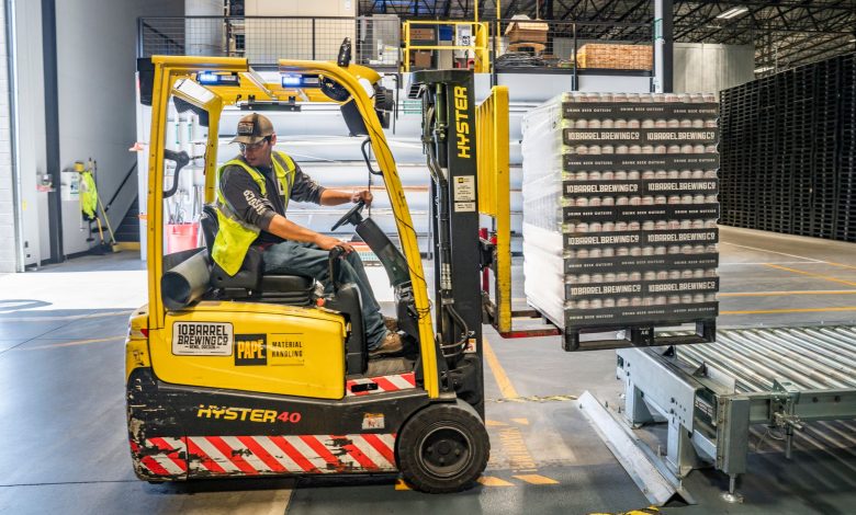 A warehouse worker maneuvers a forklift to transport crates for brewing company storage.