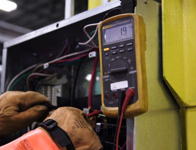 Electrician using a multimeter to test wiring in an electrical panel.