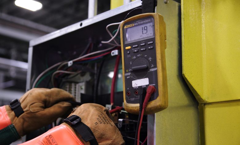 Electrician using a multimeter to test wiring in an electrical panel.