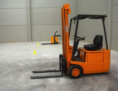An orange forklift in a spacious warehouse with concrete floors and minimal equipment.