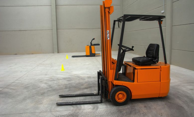 An orange forklift in a spacious warehouse with concrete floors and minimal equipment.