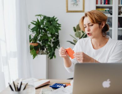 Woman reviewing bills at home desk with laptop and plants, managing personal finances.