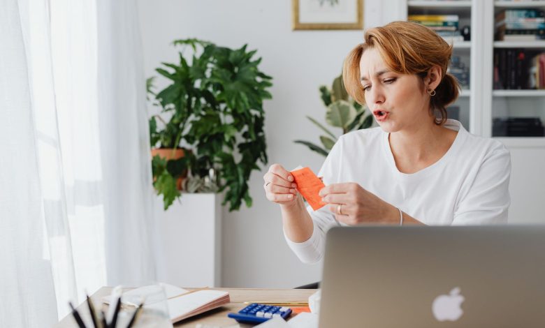 Woman reviewing bills at home desk with laptop and plants, managing personal finances.