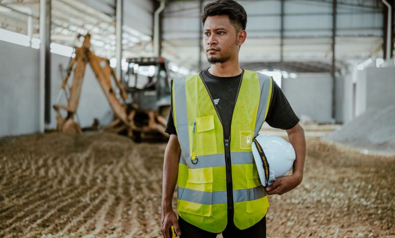 Portrait of a construction worker in safety gear holding a helmet inside an industrial setting.