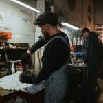 Two auto mechanics engaged in vehicle repair work inside a dimly lit garage.
