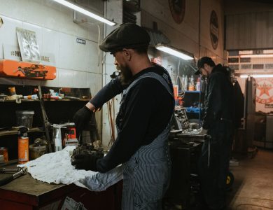 Two auto mechanics engaged in vehicle repair work inside a dimly lit garage.