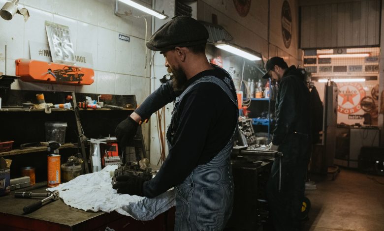 Two auto mechanics engaged in vehicle repair work inside a dimly lit garage.