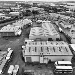 A monochrome aerial shot of an industrial area in England with warehouses and trucks.