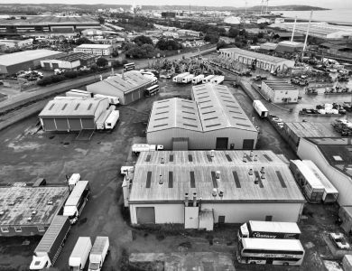 A monochrome aerial shot of an industrial area in England with warehouses and trucks.
