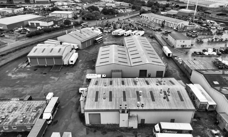 A monochrome aerial shot of an industrial area in England with warehouses and trucks.