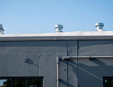Exterior of a gray industrial building with rooftop vents under a clear blue sky.